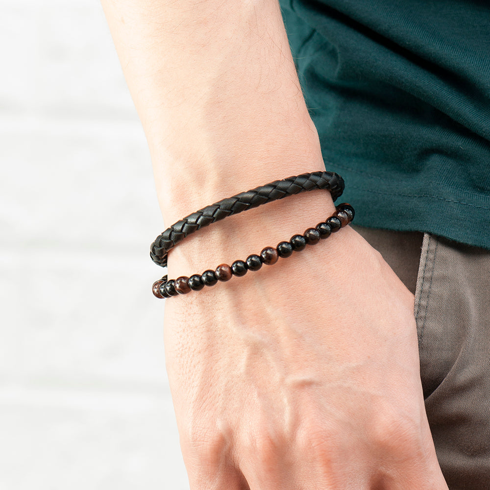 Bracelet with braided design and wooden beads on a wrist against a plain background