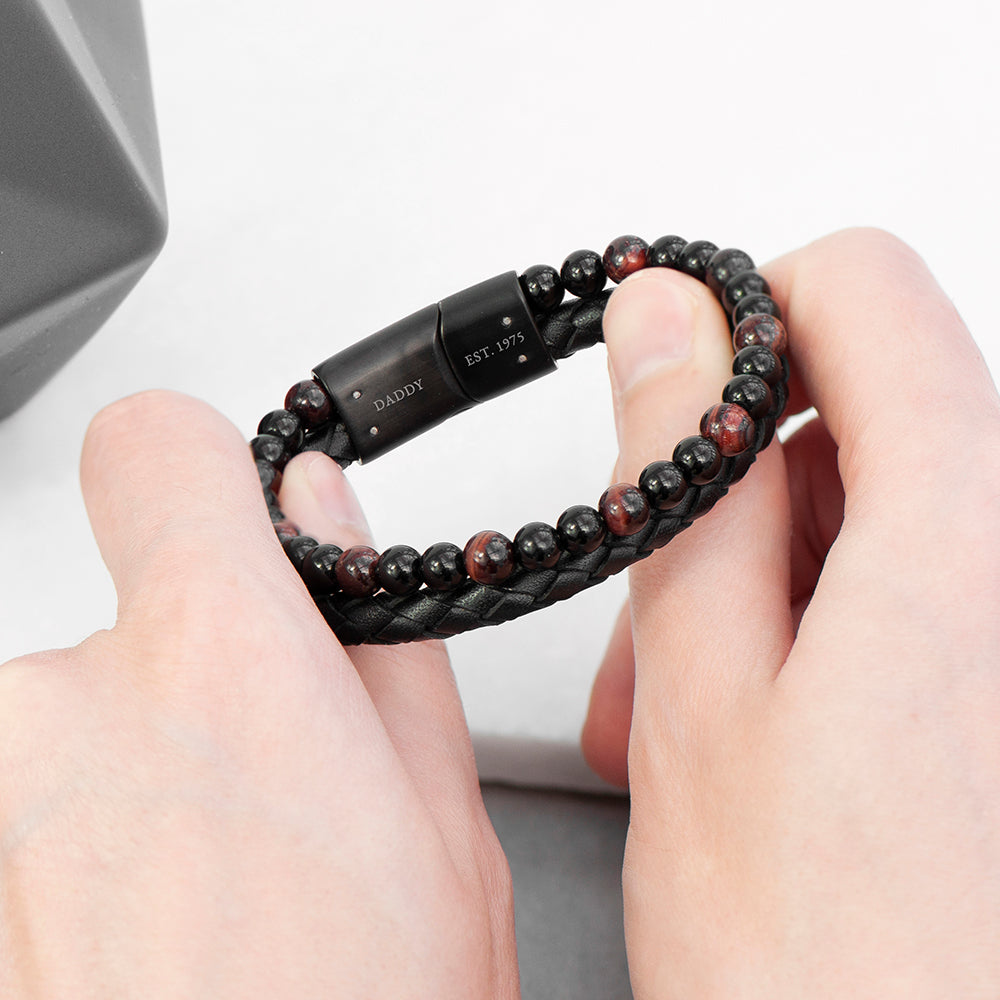 Bracelet with black and red beads and a black clasp held between two hands on a light gray background.