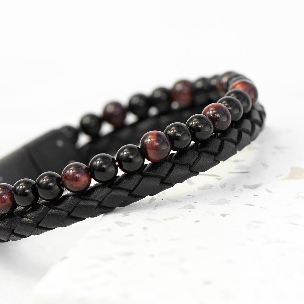 Black braided leather bracelet with red and black beaded design on a white background