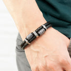 Black braided leather bracelet with silver accents on a wrist against a neutral background