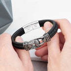 Black leather bracelet with silver clasp held by hands on a light background