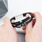 Black leather bracelet with silver beads held by hands on a light gray background