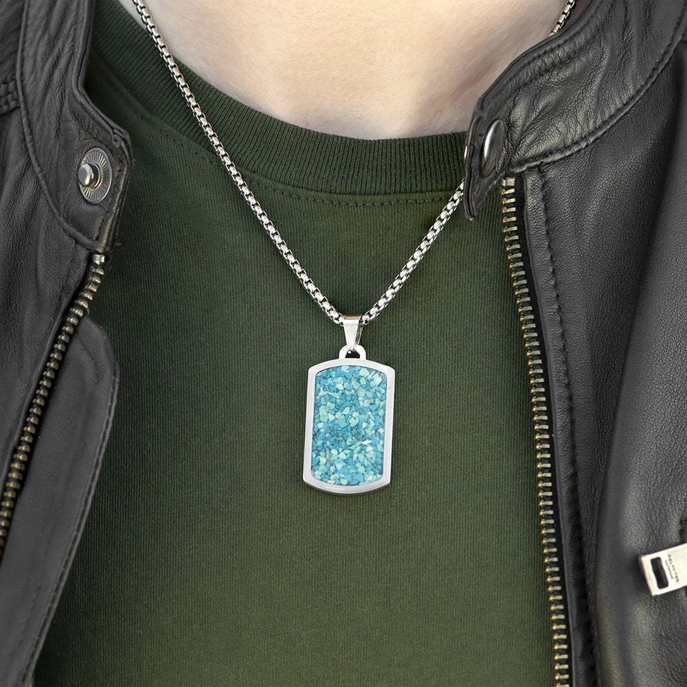Person wearing a green shirt with a black leather jacket, featuring a necklace with a blue glittery pendant.