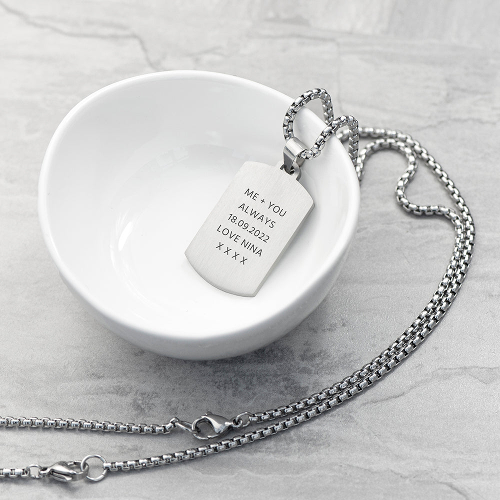 Silver necklace with a engraved tag on a white dish