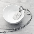 Silver necklace with a engraved tag on a white dish