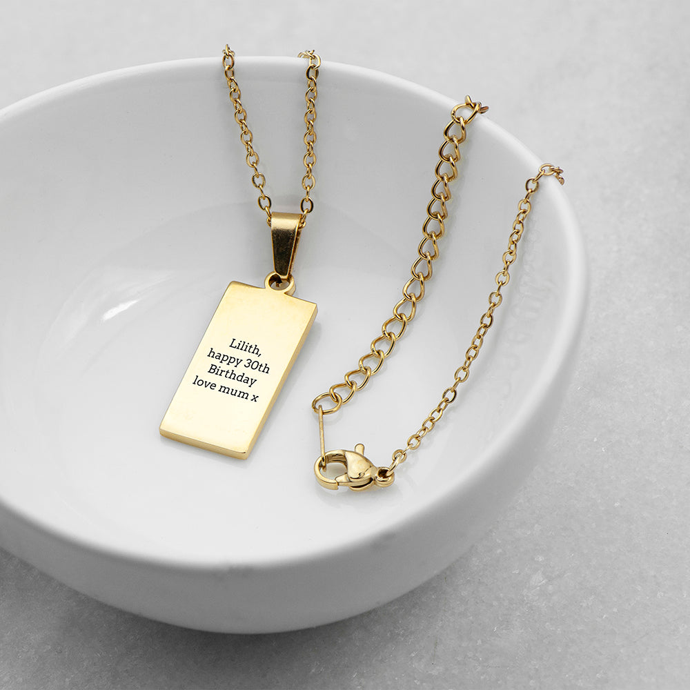 Gold necklace with a rectangular pendant on a white dish