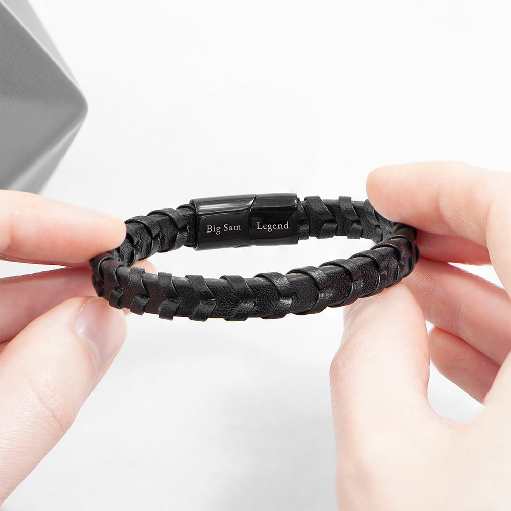 Black braided bracelet with engraved text held by hands on a white background