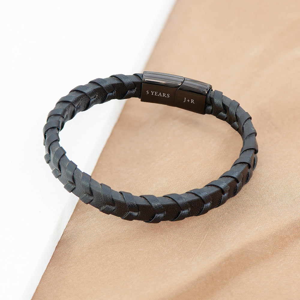 Black braided bracelet with a metal clasp on a beige surface
