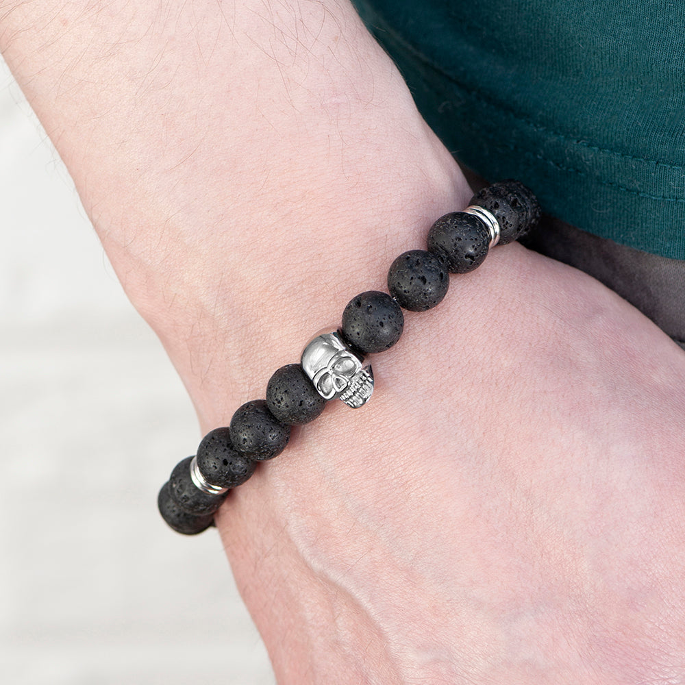 Bracelet with black beads and a silver skull charm on a wrist against a white background