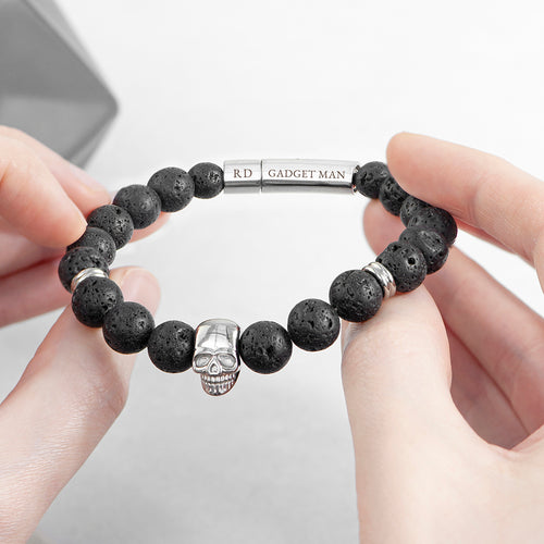 Black beaded bracelet with skull charm held by hands on a light gray background