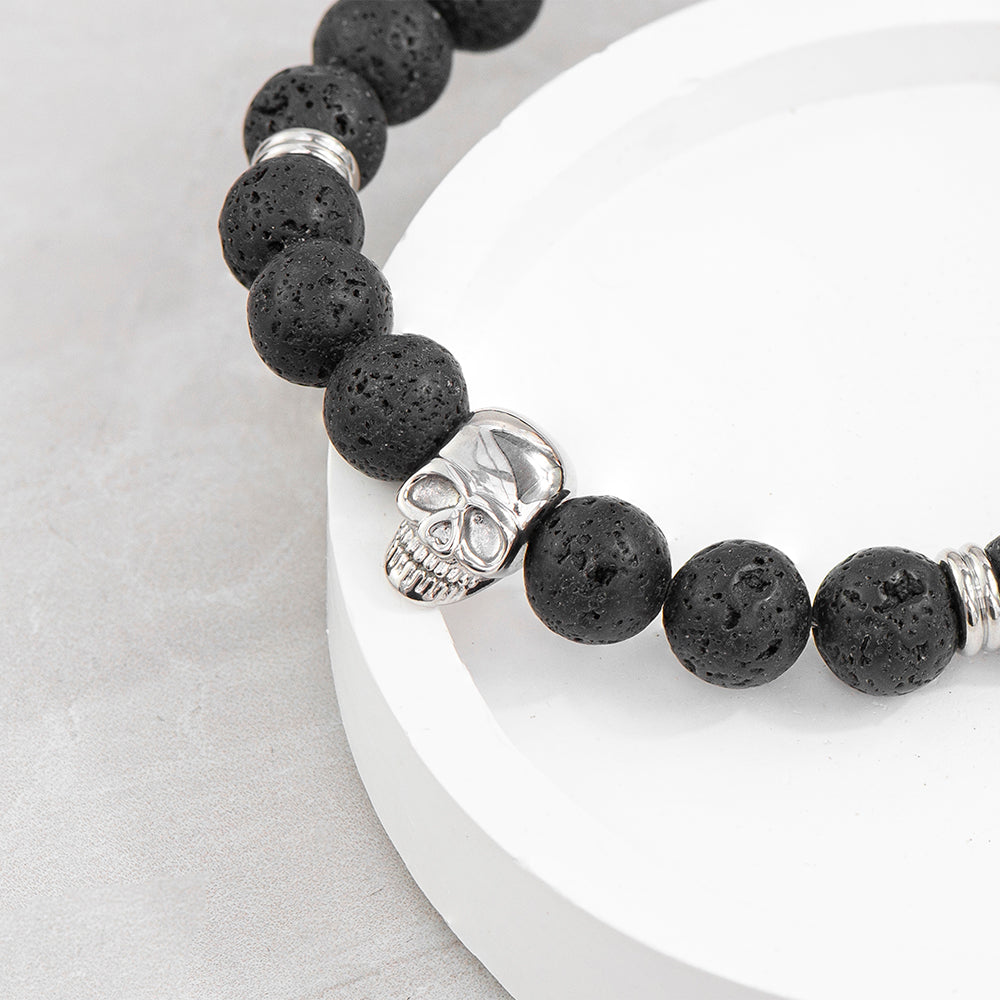 Black beaded bracelet with a silver skull charm on a white plate