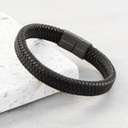 Black braided bracelet with a clasp on a light gray background