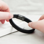 Black braided bracelet being held by a person on a light background