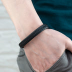 Close-up of a hand wearing a black braided bracelet on a neutral background
