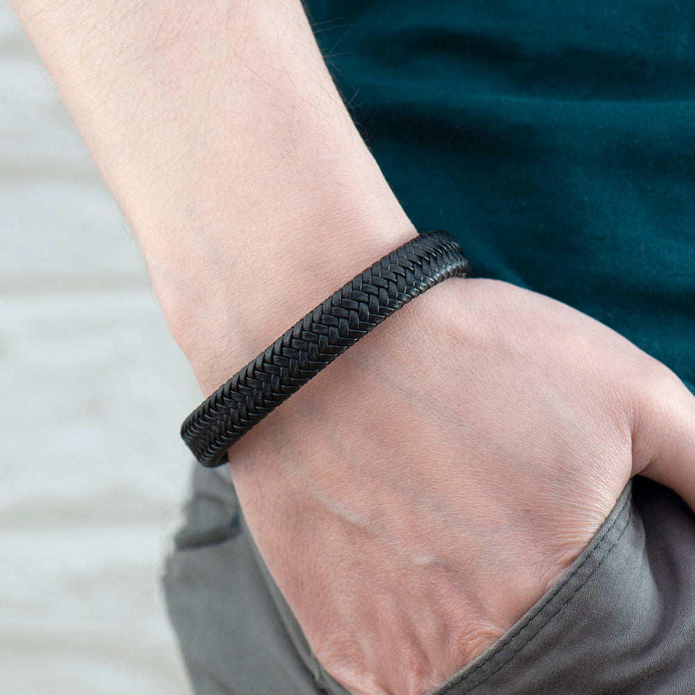 Close-up of a hand wearing a black braided bracelet on a neutral background