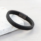 Black braided bracelet with engraved text on a light gray background
