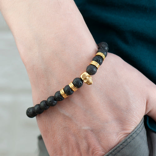 Bracelet with black beads and gold accents on a wrist against a neutral background