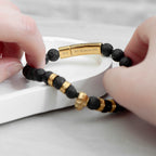 Black beaded bracelet with gold accents held by hands on a light background