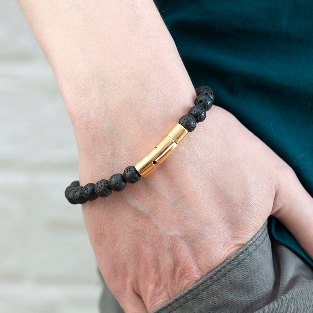 Bracelet with black beads and gold bar on a wrist against a neutral background