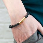 Bracelet with black beads and gold bar on a wrist against a neutral background