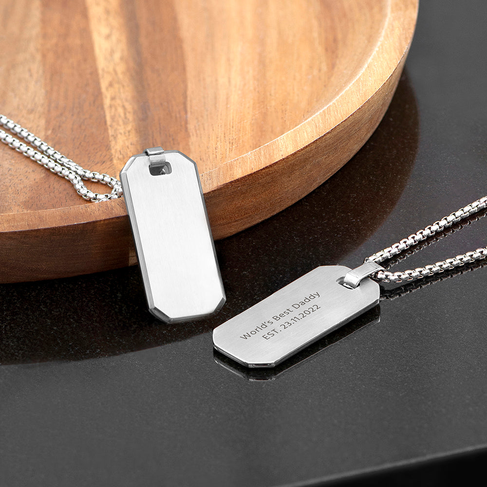 Two silver dog tags on a dark surface with a wooden circular object in the background