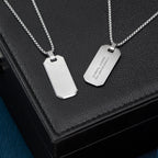 Two silver dog tag necklaces on a black leather surface