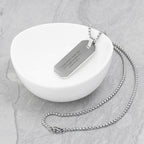 Silver necklace with an engraved tag on a white dish
