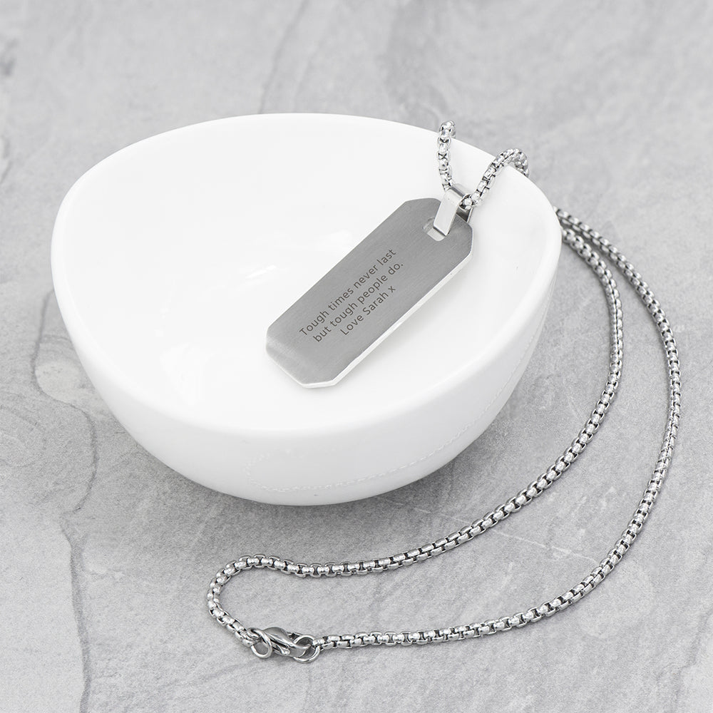 Silver necklace with an engraved tag on a white dish
