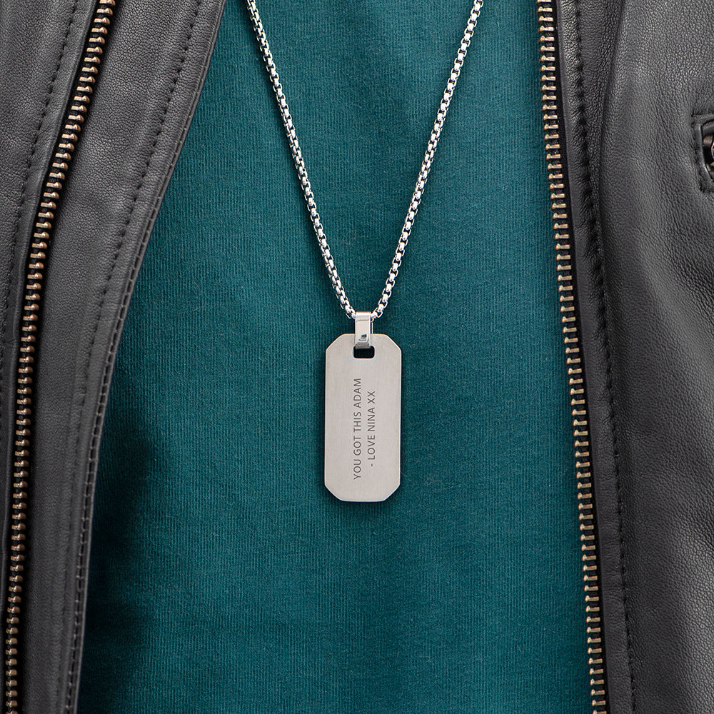 Silver dog tag necklace on a green jacket with visible text