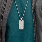 Silver dog tag necklace on a green jacket with visible text