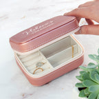 Pink jewelry box with 'Helena's treasure' inscription, containing a ring and earring, on a light surface.