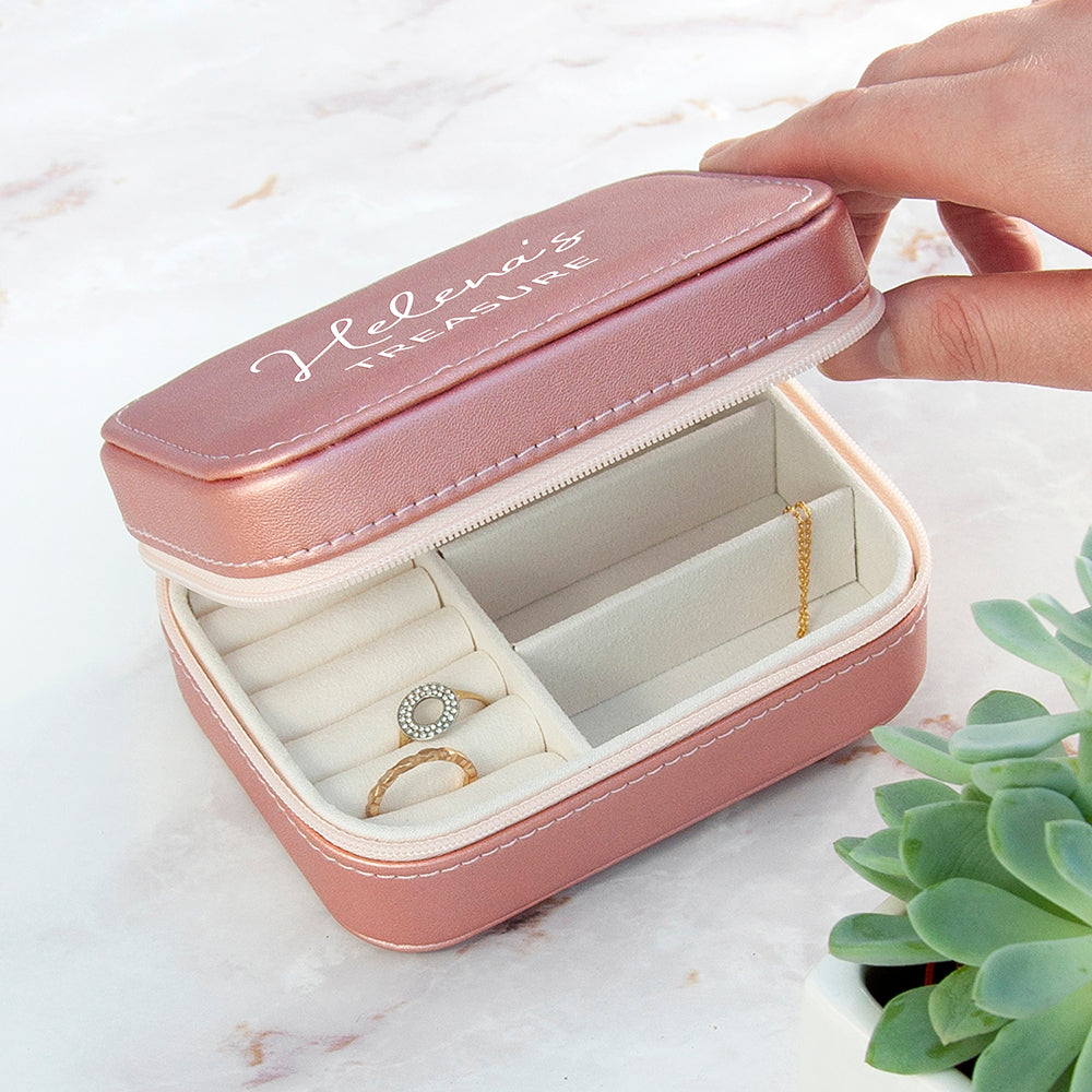 Pink jewelry box with 'Helena's treasure' inscription, containing a ring and earring, on a light surface.
