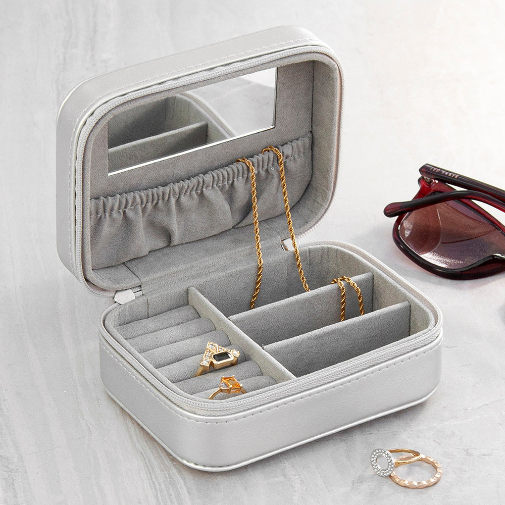 Gray jewelry box with compartments containing gold necklaces and rings, on a light wooden surface.