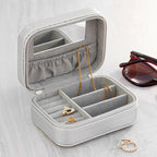 Gray jewelry box with compartments containing gold necklaces and rings, on a light wooden surface.