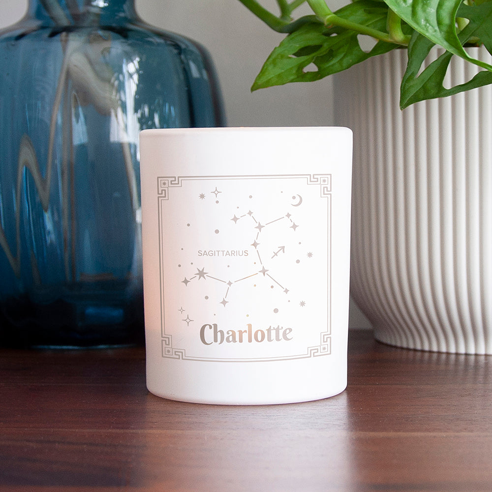 White candle with floral design and 'Mummy' text on a wooden surface, with a blue vase and plant in the background.