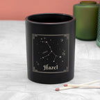 Black candle with 'Hazel' and a Virgo constellation design on a light surface.