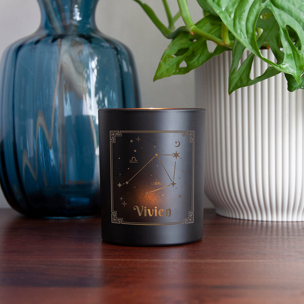 Black candle with 'Vivien' branding on a wooden surface with decorative items.