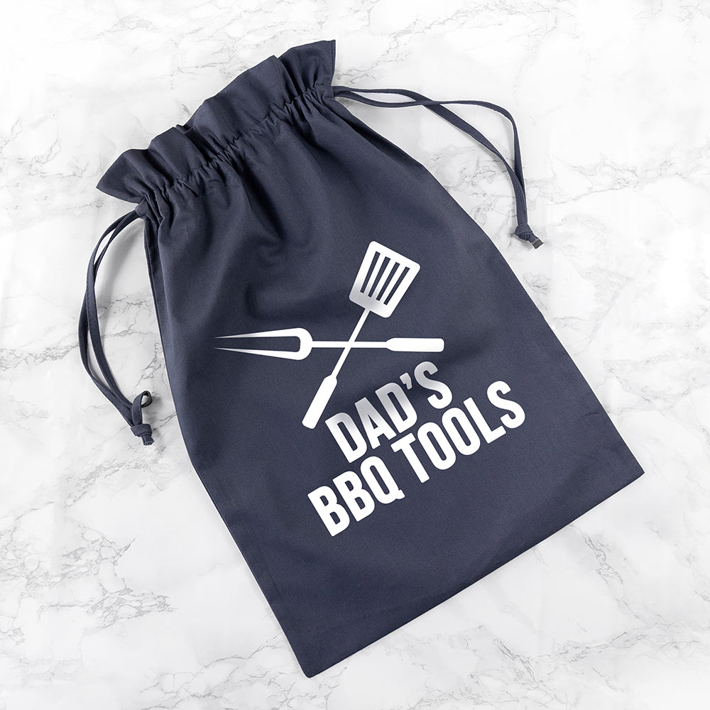 Navy drawstring bag with 'Dad's BBQ Tools' text and utensil graphics on a marble surface