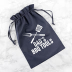 Navy drawstring bag with 'Dad's BBQ Tools' text and utensil graphics on a marble surface