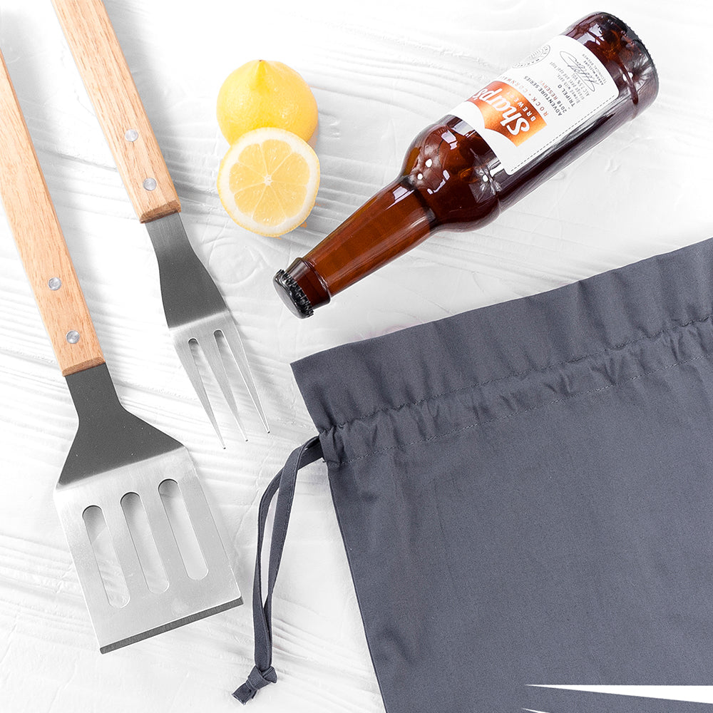 Barbecue utensils, lemons, a bottle of beer, and gray shorts on a white surface