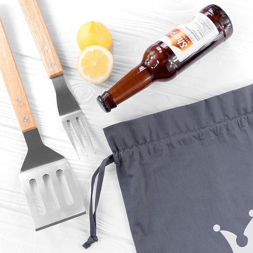 Barbecue utensils, lemons, and a beer bottle on a white surface with a gray apron.