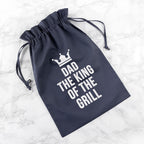 Navy drawstring bag with 'Dad, The King of The Grill' text on a marble background