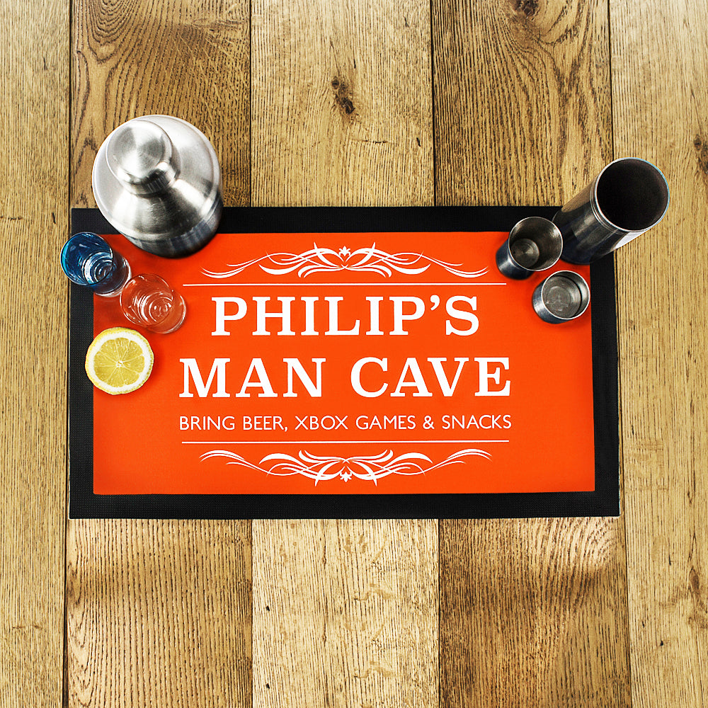 Personalized bar mat with 'PHILIP'S MAN CAVE' text on a wooden surface with bar accessories.