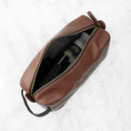 Brown leather toiletry bag with a black interior on a white background