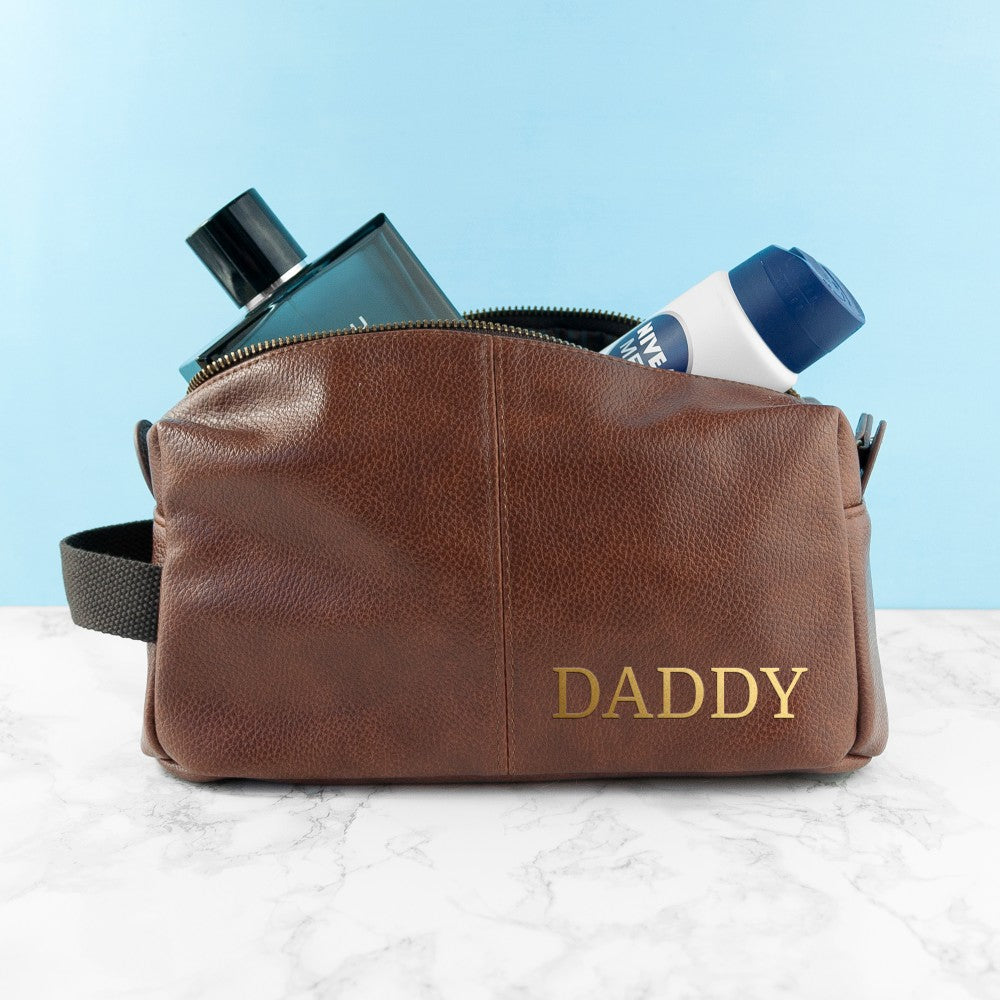 Brown leather toiletry bag with 'DADDY' engraving on a light blue background