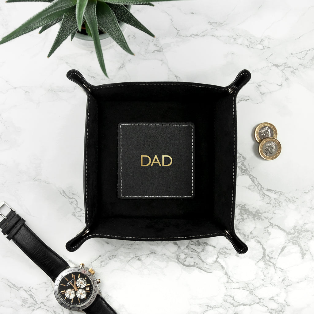 Black leather tray with 'DAD' engraving on a marble surface with a watch and coins.