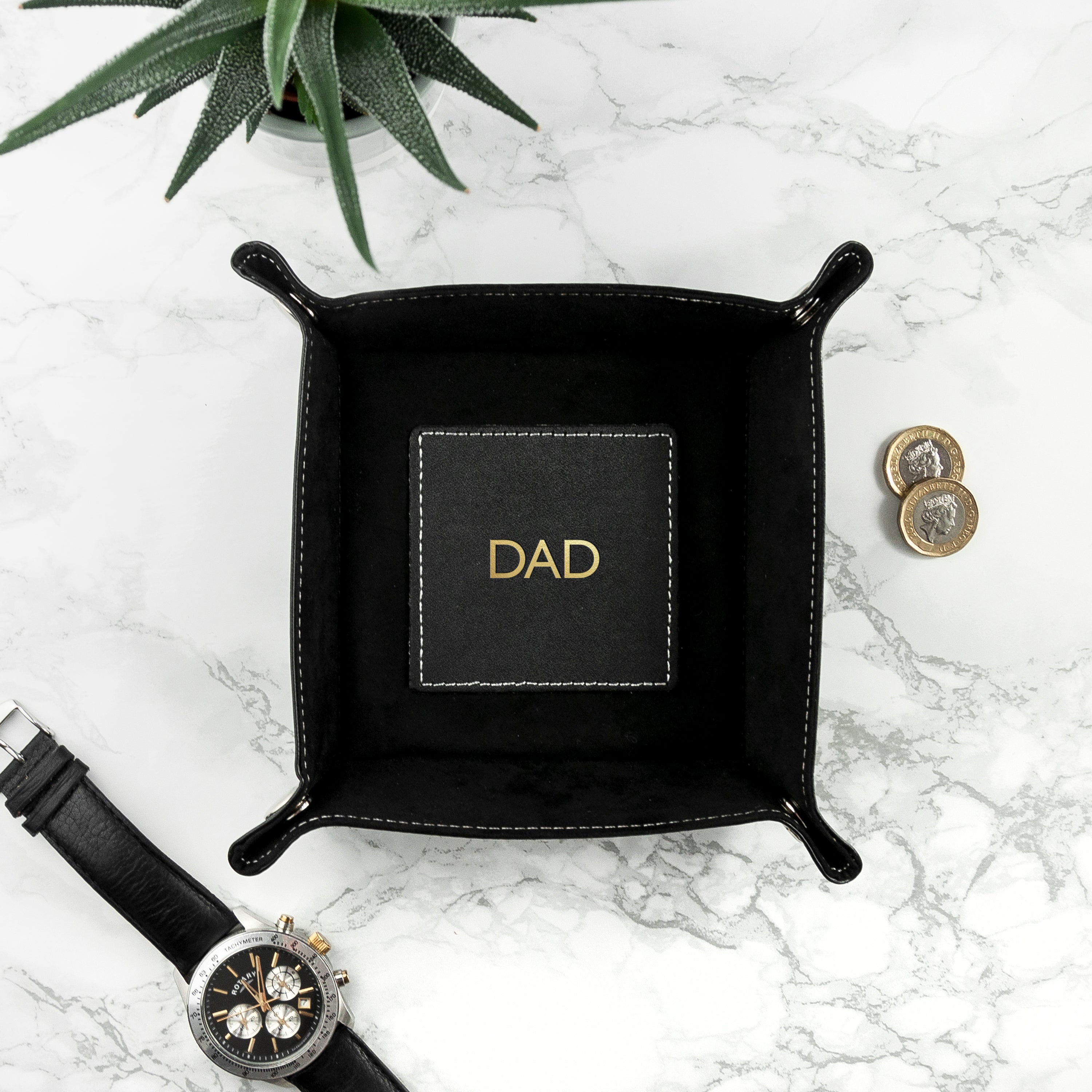 Black leather tray with 'DAD' engraving on a marble surface with a watch and coins.