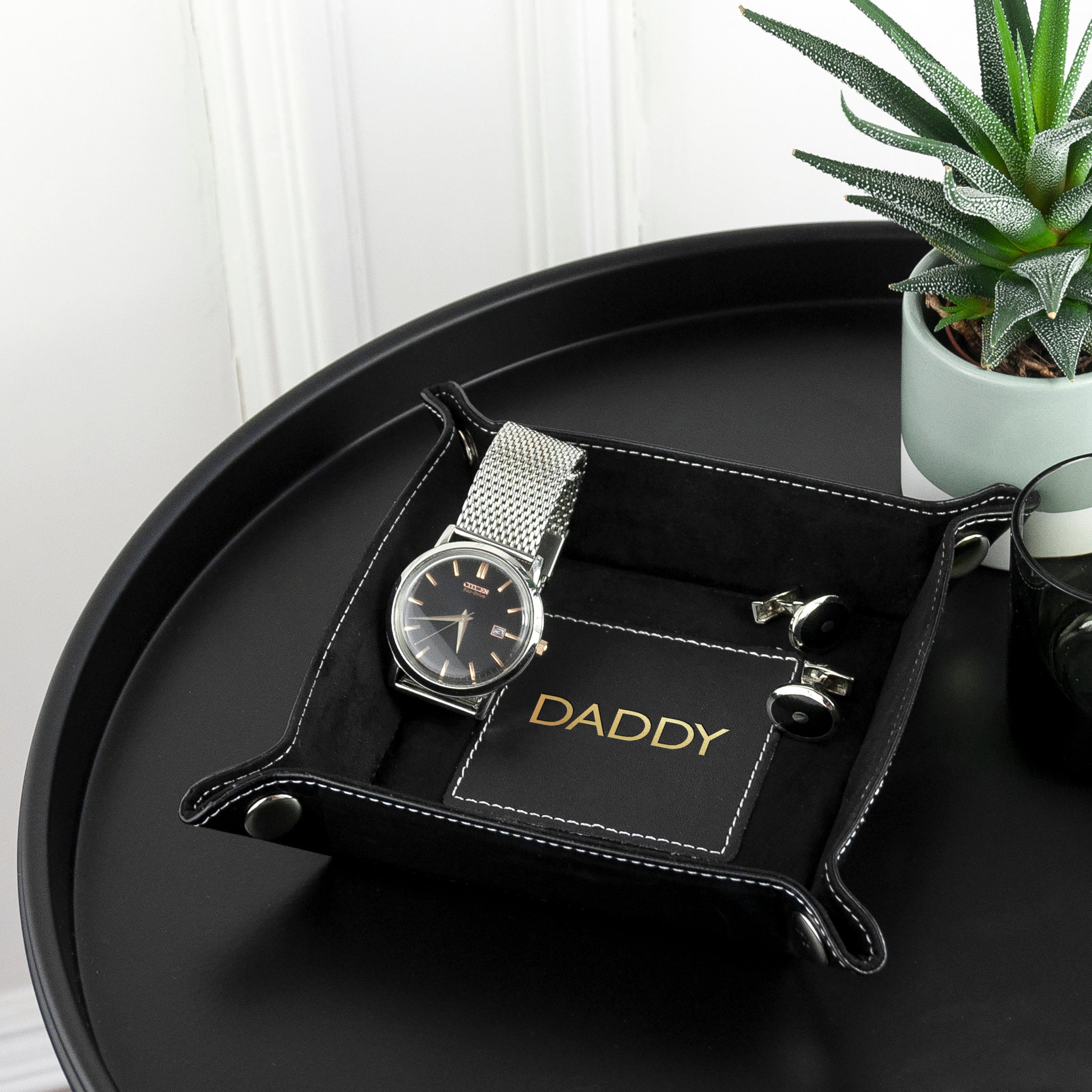 Silver watch on a black tray with 'DADDY' card, potted plant in the background