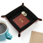 Black leather tray with a brown leather patch displaying 'POPS' next to a blue mug and notebook on a white background