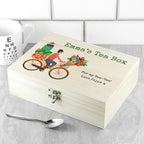 Wooden tea box with bicycle and flowers illustration, personalized text, on a tiled surface with a spoon.